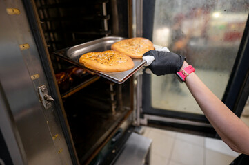 A person wearing a black glove is placing a tray of freshly baked bread into an industrial oven....
