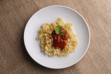 Macaroni with vegan pasta sauce a la Bolognese made from red lentils, on a white plate, brown cloth background