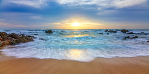 Dreamy dawn landscape on beautiful beach with waves crashing on the shore creating silk-like streaks of different shapes piercing the rock. It was great and impressive to watch the sunrise here