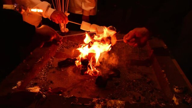 Roasting marshmallows on skewers in fire at night