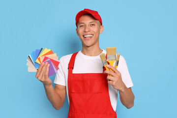 Portrait of young decorator with color palettes and brushes on light blue background