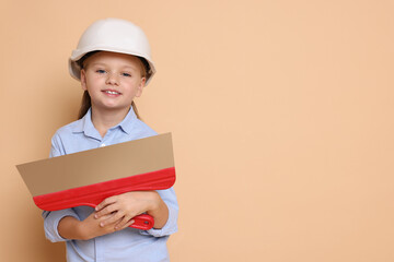 Little girl in hard hat with putty knife on beige background, space for text. Dreaming about future...