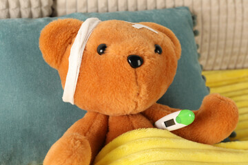 Cute teddy bear with bandage, adhesive medical plasters and thermometer on bed