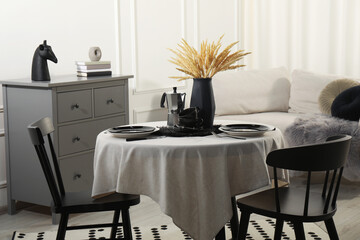 Stylish table setting with beautiful dishware and black chairs in dining room