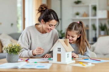other and daughter crafting a paper dream house together, representing family creativity, real estate and home ownership themes in a cozy and nurturing environment.