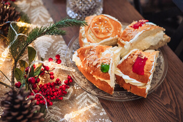 Close-up of a traditional Christmas with cream filling, decorated with candied fruits, almonds, and festive ornaments on a wooden table.