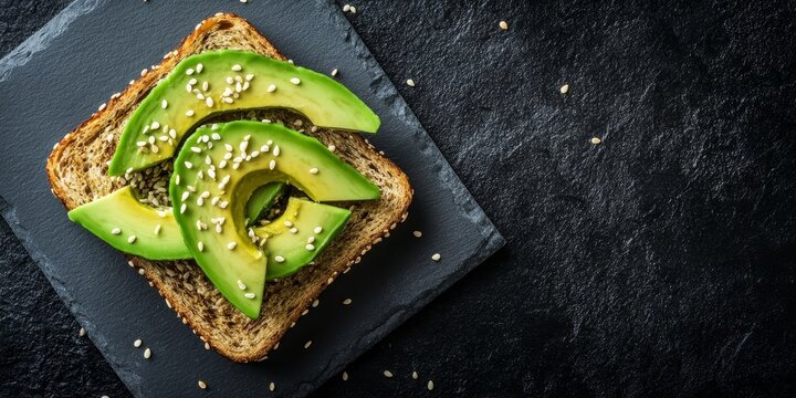 Whole grain toast topped with avocado and sprinkled with sesame seeds on a black slate background presents a vibrant, nutritious breakfast idea featuring fresh avocado.