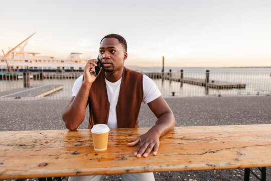 Young man talking on smartphone and drinking coffee at sunset in portugal