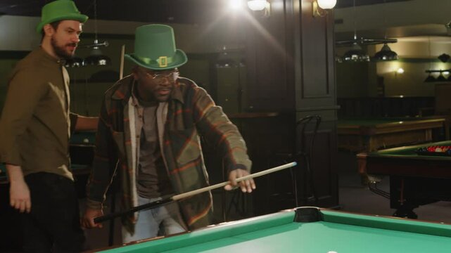 Full medium shot of diverse male friends playing rock scissors paper and starting pool in billiard club on Saint Patricks day in evening