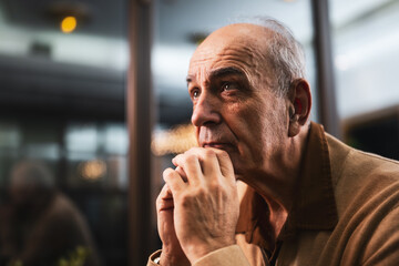 Close up portrait of pensive and worried senior man thinking about something while sitting in the...