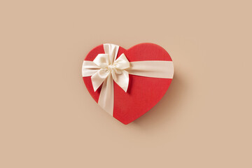 Valentines day heart shaped red gift with white bow on beige background. Top view. Greeting card.