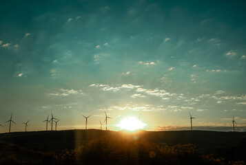 Obraz premium The sun rises over the horizon in the morning Wind turbines with propellers on horizon Energy generator on wind farm against blue sky Renewable energy