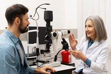 Senior female doctor performing eye exam on male patient using phoropter in ophthalmology clinic