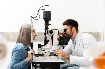 Senior woman undergoing eye exam with optometrist using slit lamp