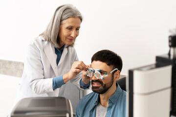 Senior female optician examining patient's eyesight with phoropter during eye exam
