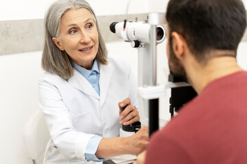 Senior female doctor performing eye exam on male patient using phoropter