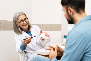 Fototapeta premium Senior female ophthalmologist explaining eye anatomy to patient using model