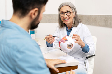 Obraz premium Senior female ophthalmologist explaining eye anatomy to patient using plastic model