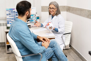 Obraz premium Senior ophthalmologist explaining eyesight problems to male patient using anatomical model of eye