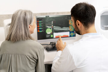 Ophthalmologist showing medical exam results on computer to senior patient