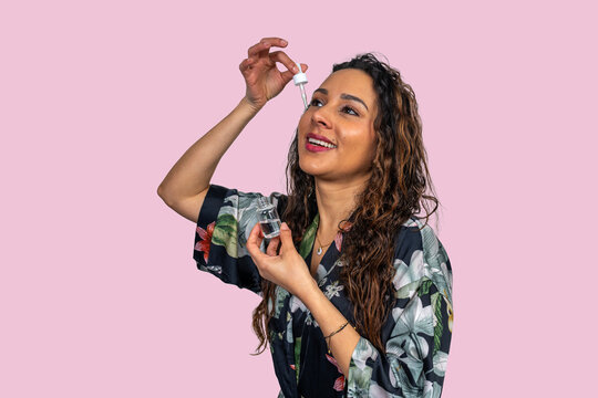 Smiling woman applying face serum with dropper on pink background