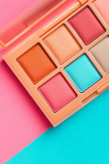 Brightly colored makeup palette displays blush tones against pink and turquoise backdrop