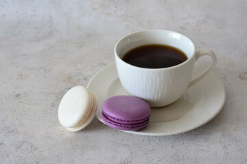 a cup of coffee next to two white and purple macaroons close up