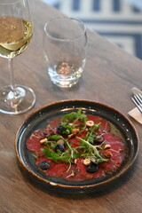 Beef carpaccio with arugula and blueberries on a wooden table