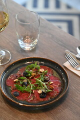 Beef carpaccio with arugula and blueberries on a wooden table