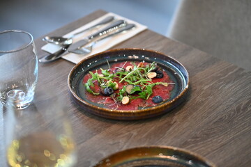 Beef carpaccio with arugula and blueberries on a wooden table