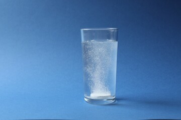 Effervescent pill dissolving in a glas water on blue background 