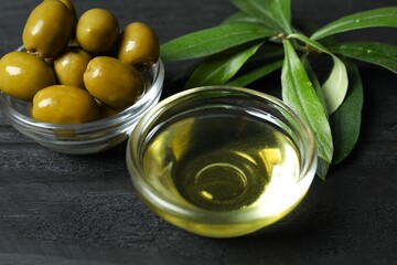 Bowl of fresh olive oil and olives with leaves on wooden background