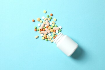 Various pills pouring out of medicine bottle on color background