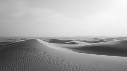 Waves of sand stretch across an empty desert landscape under a soft gray sky at dusk, creating a peaceful and tranquil ambiance