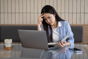 Asian businesswoman feeling stressed in coffee shop using digital laptop to work online