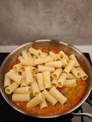 Rigatoni pasta added to tomato sauce in stainless steel pan