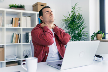Tired business man with neck pain looking uncomfortable while working with laptop in a modern...