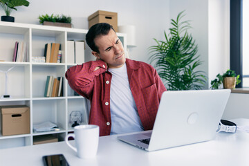 Tired business man with neck pain looking uncomfortable while working with laptop in a modern...