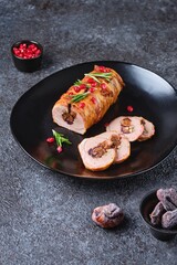 Ready-made pork tenderloin roll with figs and walnuts, wrapped in bacon, on a black ceramic plate on a dark concrete background. Recipes pork.