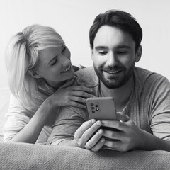 Monochrome bw image - couple lying on bed browsing internet reading text message use cellphone cell phone cellular device. Happy bearded man and woman shop online by smartphone. Technology. Square