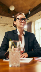 Focused young woman, employee in formal wear and glasses sitting at table during professional meeting with colleagues and leader. Concept of business, workshop, professional development