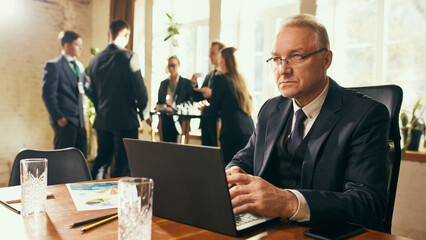 Serious and focuses businessman in his 50s sitting at tale in office and typing on laptop. Working with concentration and workshop creating strategies. Concept of business, professional development