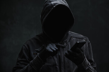 Hooded computer hacker using smartphone