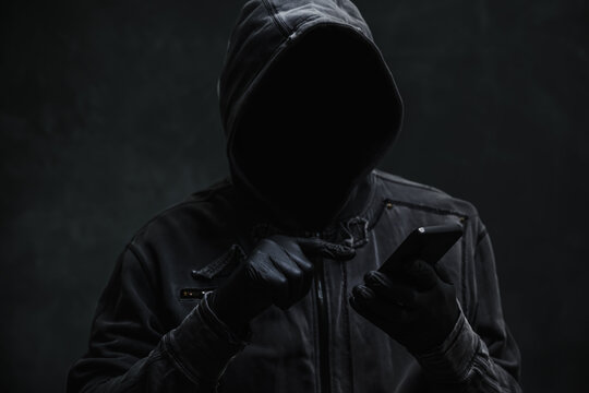 Hooded computer hacker using smartphone