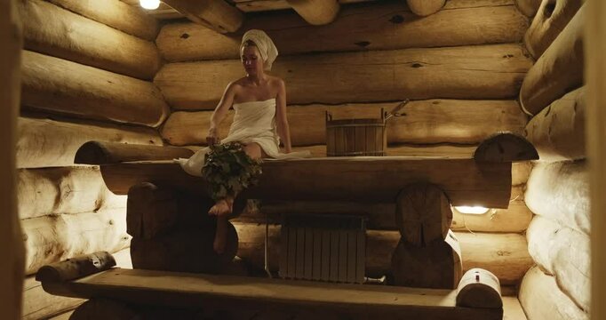 Woman relaxing and sweating in Russian bath house in towel. Girl In Spa. Interior of Finnish sauna. Classic wooden bathhouse with hot steam. Russian sauna. Relax in hot bath house. Classic bathhouse