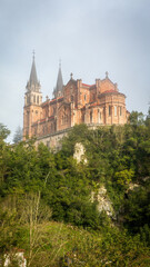 Fototapeta premium The stunning Basilica of Covadonga, perched on a hillside in the Picos de Europa mountains, enveloped by lush greenery and mist, is a symbol of Spanish religious heritage