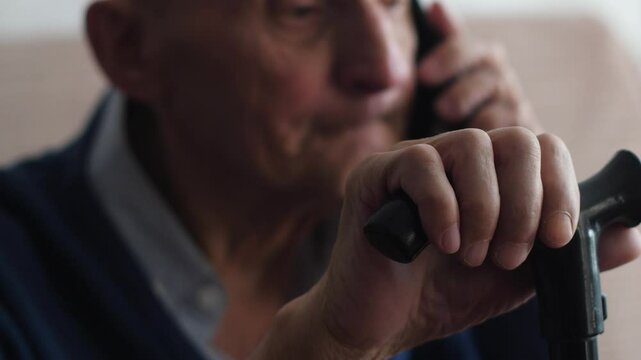elderly man 75 years old talking on phone sitting holding walking stick with hand real pensioner everyday life