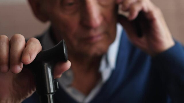 elderly man 75 years old talking on phone sitting holding walking stick with hand real pensioner everyday life