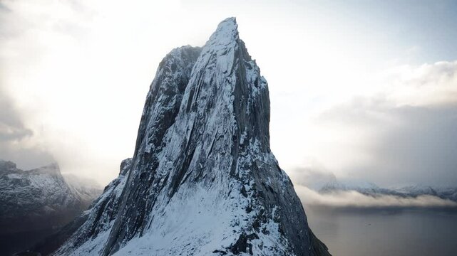 Handheld shot of a person walking up to the base of Segla mountain on the island of Senja in the Arctic Circle of Northern Norway.  A snow=capped mountain peak in the fall.