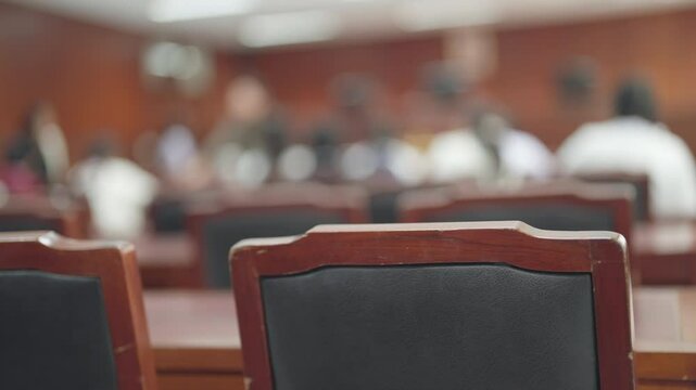 A blurry image of a classroom with a wooden chair in the foreground. The chair is black and has a wooden back. The image is blurry, giving it a sense of motion and energy